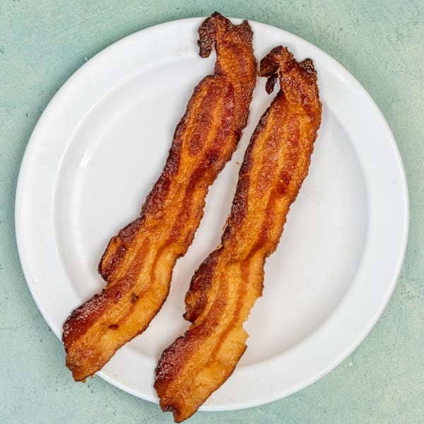 Two crispy strips of bacon on a white plate from Ellen's Kitchen, ready for breakfast.