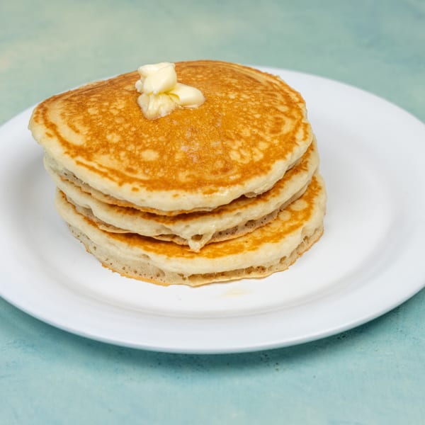 Stack of golden pancakes topped with melting butter on a white plate at Ellen's Kitchen.