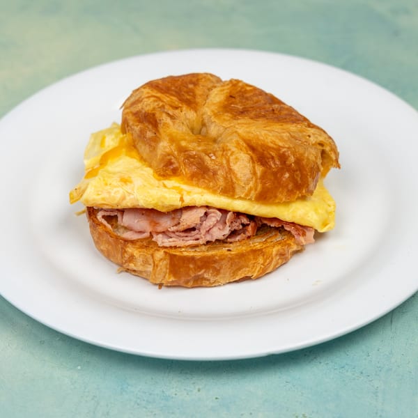A golden croissant breakfast sandwich with scrambled eggs and ham on a white plate.