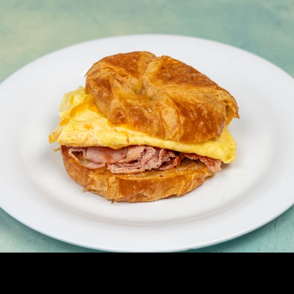 A golden croissant breakfast sandwich with scrambled eggs and ham on a white plate.