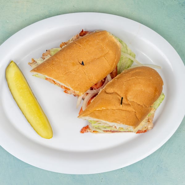A chicken sandwich cut in half with lettuce, tomato, and onion, served with a pickle spear.