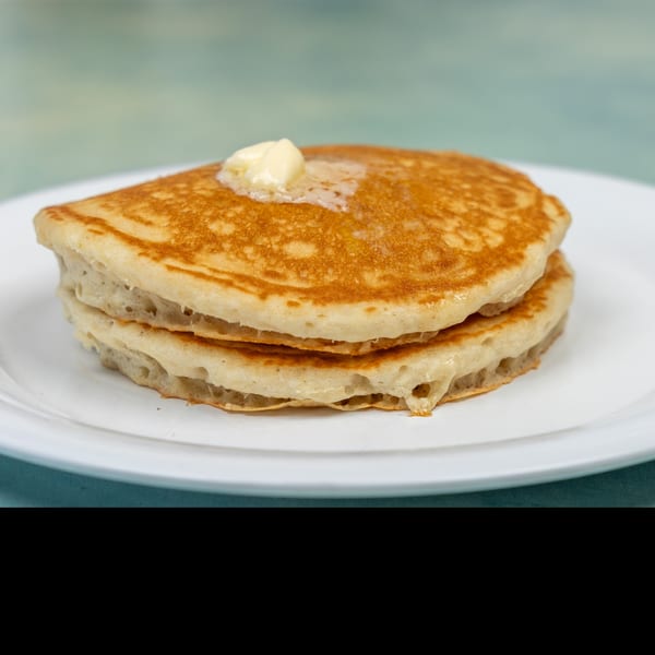 Stack of golden-brown pancakes with melting butter on a white plate from Ellen's Kitchen.